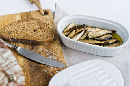 Sandwich with smoked sprats in oil, ceramic jar, wooden cutting Board with black bread. White background, top viewの写真素材