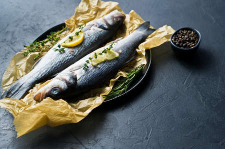 Raw sea bass with rosemary, thyme and lemon. Black background, top view, space for text