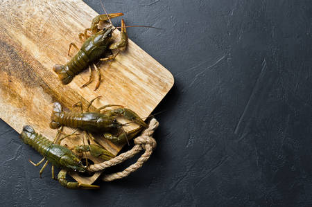 Live crayfish run away from the wooden chopping Board. Black background, top view, space for text