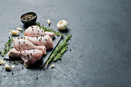 Raw chicken legs. Ingredients for cooking: rosemary, thyme, garlic, pepper. Black background, top...