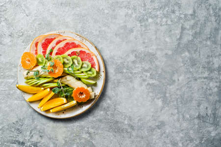 Assorted fruit on a plate, restaurant. Grapefruit, tangerine, kiwi, orange, banana, Apple. Gray...