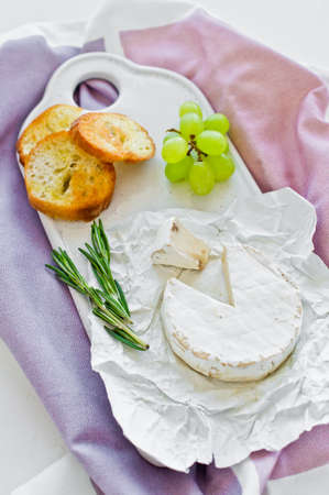 Brie cheese with nuts on a white cutting Board, grapes, rosemary. White background, top view