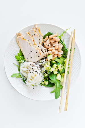 Buddha bowl with glass noodles, beans, chicken breast, spinach, arugula and cucumber. White background, top view, space for textの写真素材