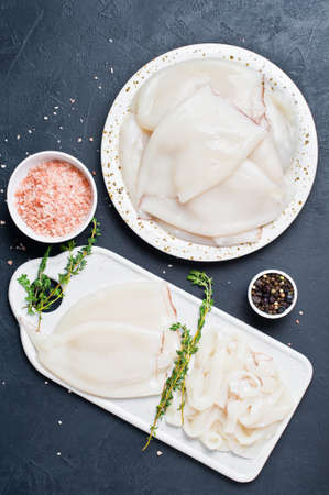Whole raw squid and cut into rings on a cutting Board. Ingredients for cooking - thyme, pepper, pink...