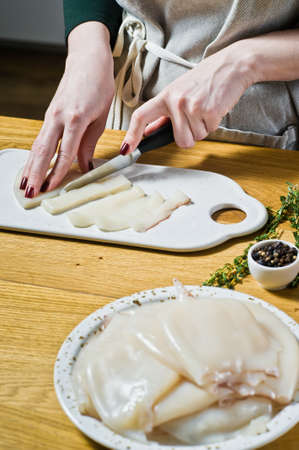 The chef cuts raw squid into rings on the cutting Board. Black background, side view, kitchenの写真素材