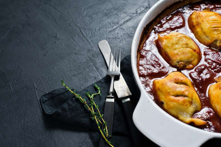 Stuffed baked squid in tomato sauce. Black background, top view, space for text