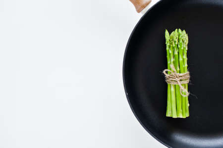 Bunch of green mini asparagus in a pan. White background, top view, space for textの写真素材