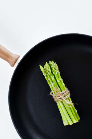 Bunch of green mini asparagus in a pan. White background, top view, space for textの写真素材