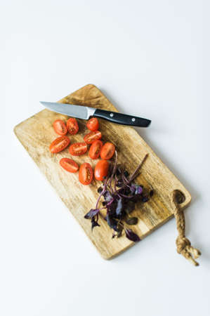 Cherry tomatoes and Basil on a wooden chopping Board. Top view, white backgroundの写真素材