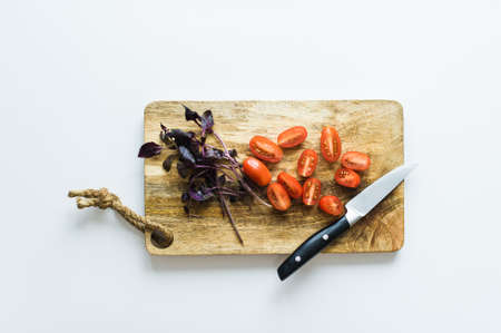 Cherry tomatoes and Basil on a wooden chopping Board. Top view, white backgroundの写真素材