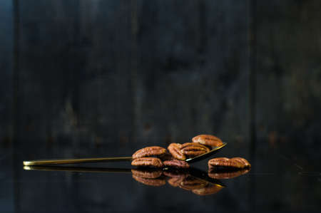 Pecan in a spoon on a mirror, black background, side view