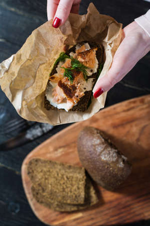 The hands of the chef holding the Scandinavian sandwich with smoked salmon on black bread with soft...