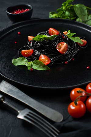 Vegetarian dish, black spaghetti with Basil and cherry tomatoes. Black background, top viewの写真素材
