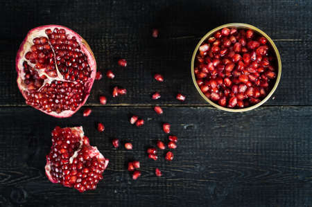 Ripe pomegranate, pomegranate kernels on black wooden background