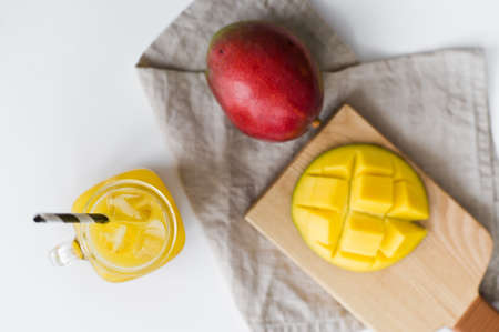 Ripe mango, half mango and a glass of mango juice with a tube on a wooden cutting Boardの写真素材