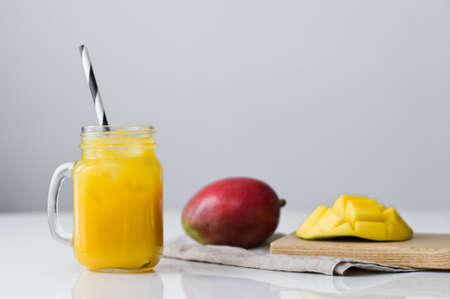 Ripe mango, half mango and a glass of mango juice with a tube on a wooden cutting Boardの写真素材