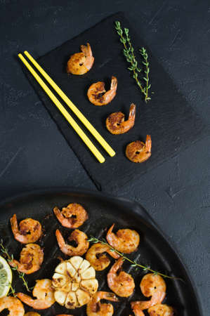 Fried king prawns in a frying pan on a black background with yellow chopsticksの写真素材