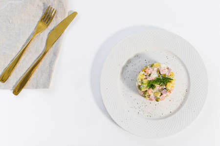 Russian salad on a white plate with a Golden knife and fork on a white backgroundの写真素材