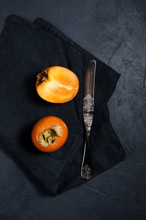 Ripe persimmon, knife on black background with space for textの写真素材
