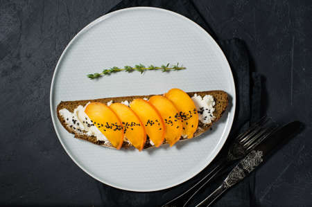 Healthy balanced food sandwich with persimmon and soft cheese on black backgroundの写真素材