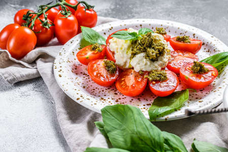 Italian cheese stracciatella (mozzarella buffalo) on small plate served with fresh tomatoes and basil. Gray background. Space for text.の写真素材