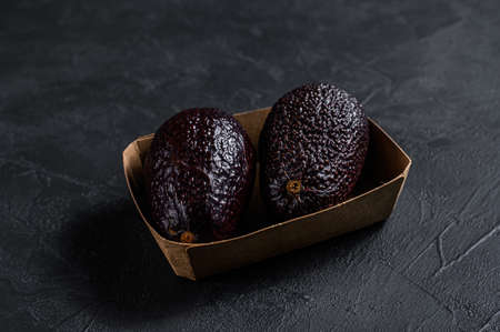 Avocado in a cardboard package from the supermarket. Black background. Top view. Space for text.