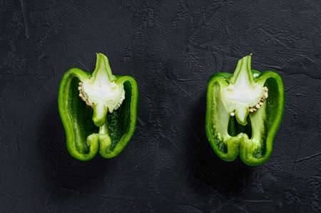 Cut green bell pepper, two halves. Black background. Top view. Space for text sweet pepper, two...
