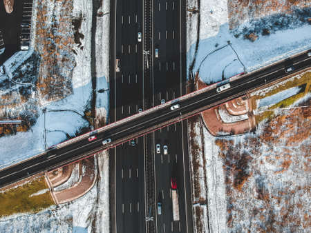Aerial view of country road and bridge, road traffic, snow-covered forests and fields, winter....
