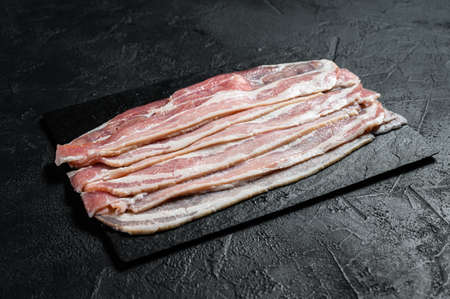 Raw bacon on a stone chopping Board. Pork meat. Black background. Top view.の写真素材