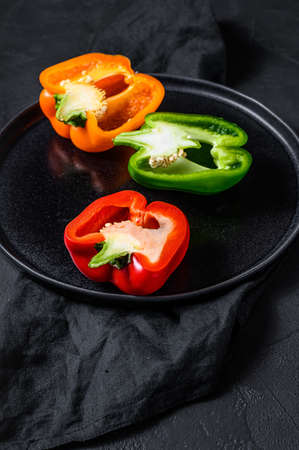 Three cut orange, green and red sweet peppers. Black background. Top view.