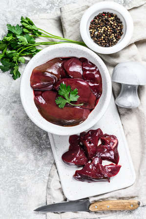 Raw chicken liver in a bowl. Gray background. Top view.
