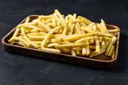 Frozen French fries in a wooden bowl. organic potatoes. Black background. Top view. Space for text.