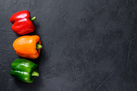Green, orange and red bell peppers. Black background. Top view. Space for text