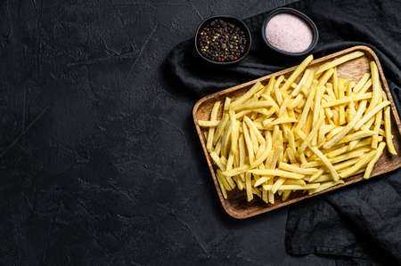 Frozen French fries in a wooden bowl. organic potatoes. Black background. Top view. Space for text.