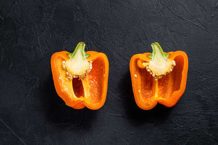 Cut orange bell pepper, two halves. Black background. Top view. Space for text