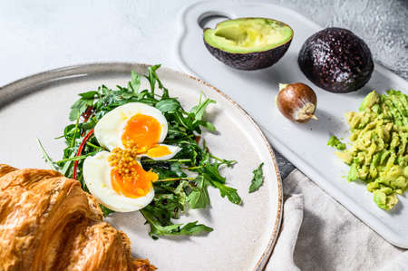 Salad with avacado, arugula, croissant and egg. Gray background. Top view.