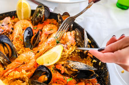 Spanish Seafood Paella Rice Dish with Fresh Shrimp, Scampi, mussels, squid, octopus and scallops Served in Pan. The waiter puts a portion on the plate. Top view. Restaurant.の写真素材