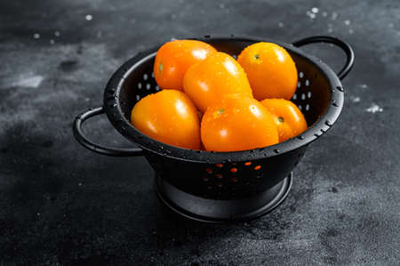 Raw fresh yellow tomatoes in a colander. Black background. Top view.の写真素材