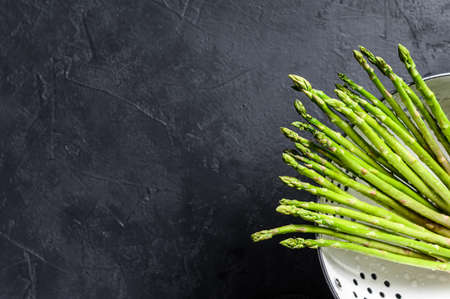 Fresh baby green asparagus in a colander. Black background. Top view. Copy space.の写真素材