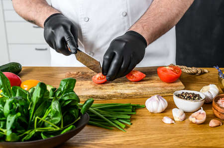 A chef in black gloves is slicing tomatoes on a wooden chopping Board.の写真素材