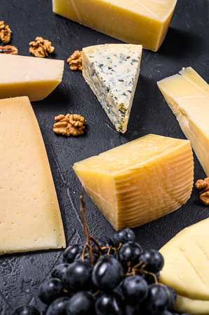 Different types of delicious cheese with walnuts and grapes. Black background. Top view.