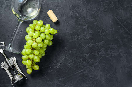 A branch of green grapes, a wine glass, a corkscrew and a cork. Concept of wine-making. Black background. Top view. Copy space.の写真素材