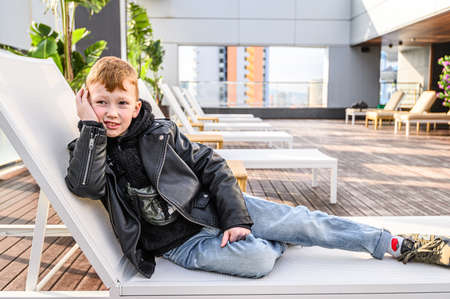 The child is lying on a sunbed by the pool. Swimming pool on roof top with beautiful city view of the skyscrapers. . Premium hotel. 03.01.2020 Barcelona, Spain.のeditorial素材