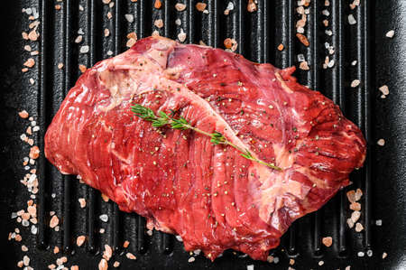 Top blade steak on a grill pan, raw meat, marbled beef . Black background. Top view.