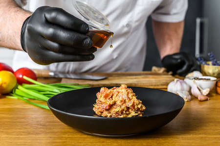 The chef in black gloves prepares tartare from fresh tuna fish.
