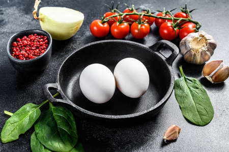 Concept of cooking Breakfast with fried or boiled eggs. Ingredients Eggs, onion, garlic, tomatoes, pepper, spinach. Black background. Top view.の写真素材