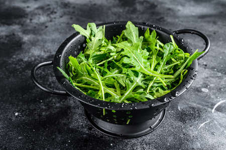 Fresh arugula leaves in a colander. Black background. Top view.の写真素材