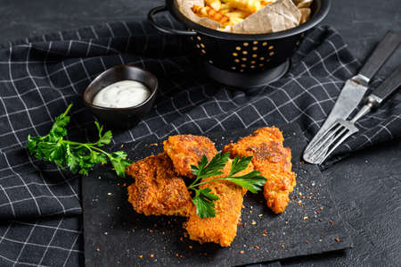 Fish and chips, French fries and cod fillet fried in breadcrumbs. Black background. Top view.