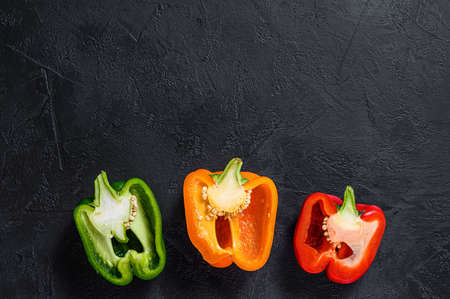 Three sliced orange, green and red bell peppers. Black background. Top view. Space for text.