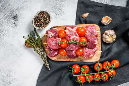 Raw beef meat kebab on cutting board. BBQ with tomato and spices. Gray background. Top view.